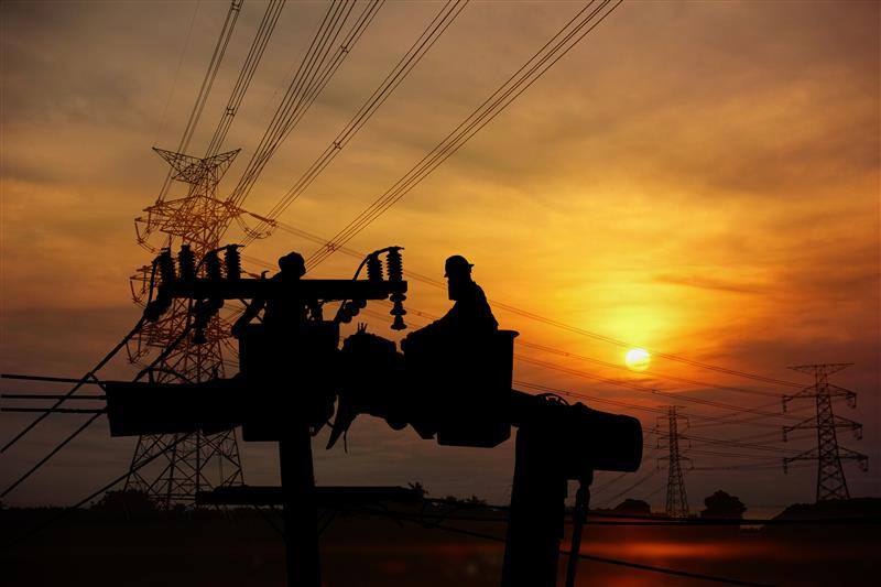Two electrician working on high-voltage lines at sunset, power line in the foreground image