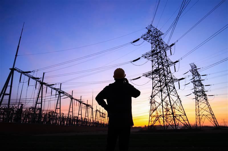 Electrician standing in front of high-voltage towers at dusk